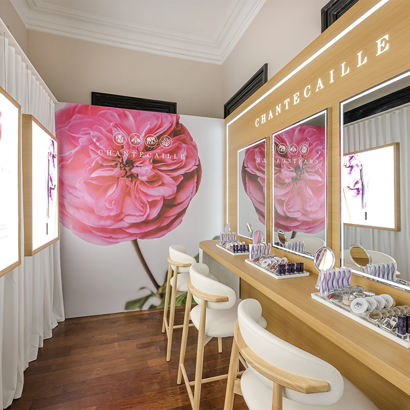 The picture shows a makeup studio with a makeup tables and mirrors on the walls. There are three make-up stations on the picture. Each station has makeup and beauty products of the brand on display. (photo)